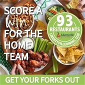 A spread of appetizers, including guacamole, pretzels, wings, and celery sticks, is organized in bowls on a table. Two hands each reach for a snack and dip. Text says "Score a win for the home team - Get Your Forks Out."